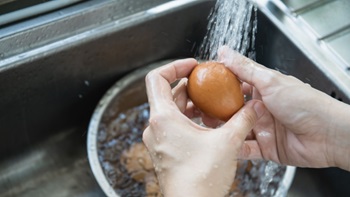 Mani che lavano un uovo sotto il rubinetto